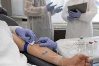 Clinicians preparing a patient's arm for a cell therapy injection in a softly lit hospital room, focused on hands and medical equipment.